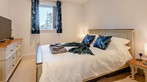 Un dormitorio con cama, mesita de noche, televisor y ventana con cortinas.