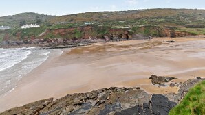 Un paisaje costero con una playa arenosa, afloramientos rocosos y una colina con vegetación.