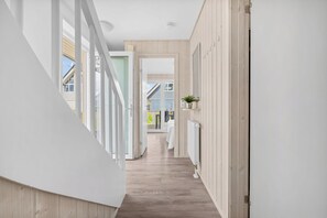 Ein Korridor mit Holzboden, weißen Wänden und einer Tür zu einem Zimmer mit Bett und Pflanze.