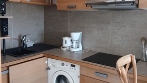 Eine kompakte Küche mit Holzschränken, einer integrierten Waschmaschine, einer Kaffeemaschine und einem Holzstuhl.