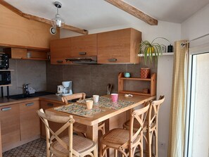 A kitchen with wooden cabinets, a coffee maker, and a dining table with chairs. - Charming studio apartment in the Cassy harbor (Lanton)