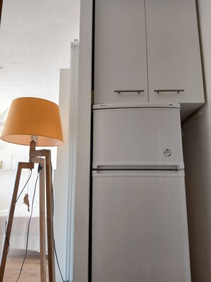 A white refrigerator with a logo, a lamp with a beige shade, and a wooden floor. - Charming studio apartment in the Cassy harbor (Lanton)
