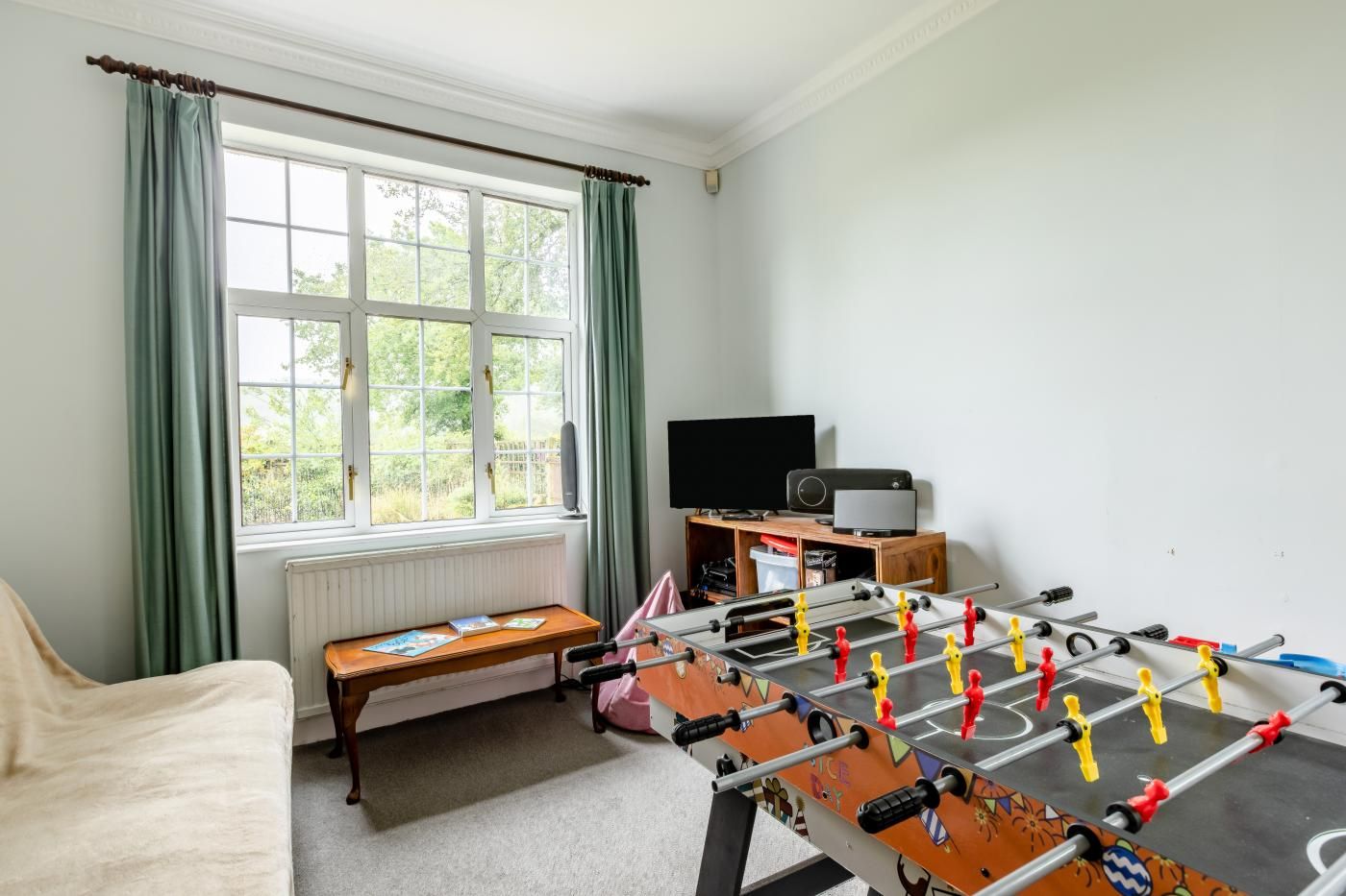 Une pièce avec une table de baby-foot, un téléviseur et une fenêtre avec des rideaux.