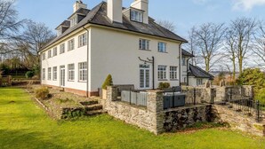 Una casa de dos pisos con base de piedra, múltiples ventanas y un césped bien cuidado.