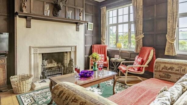 Una habitación tradicional con chimenea, un sillón rojo, un sofá estampado y vistas a la vegetación.