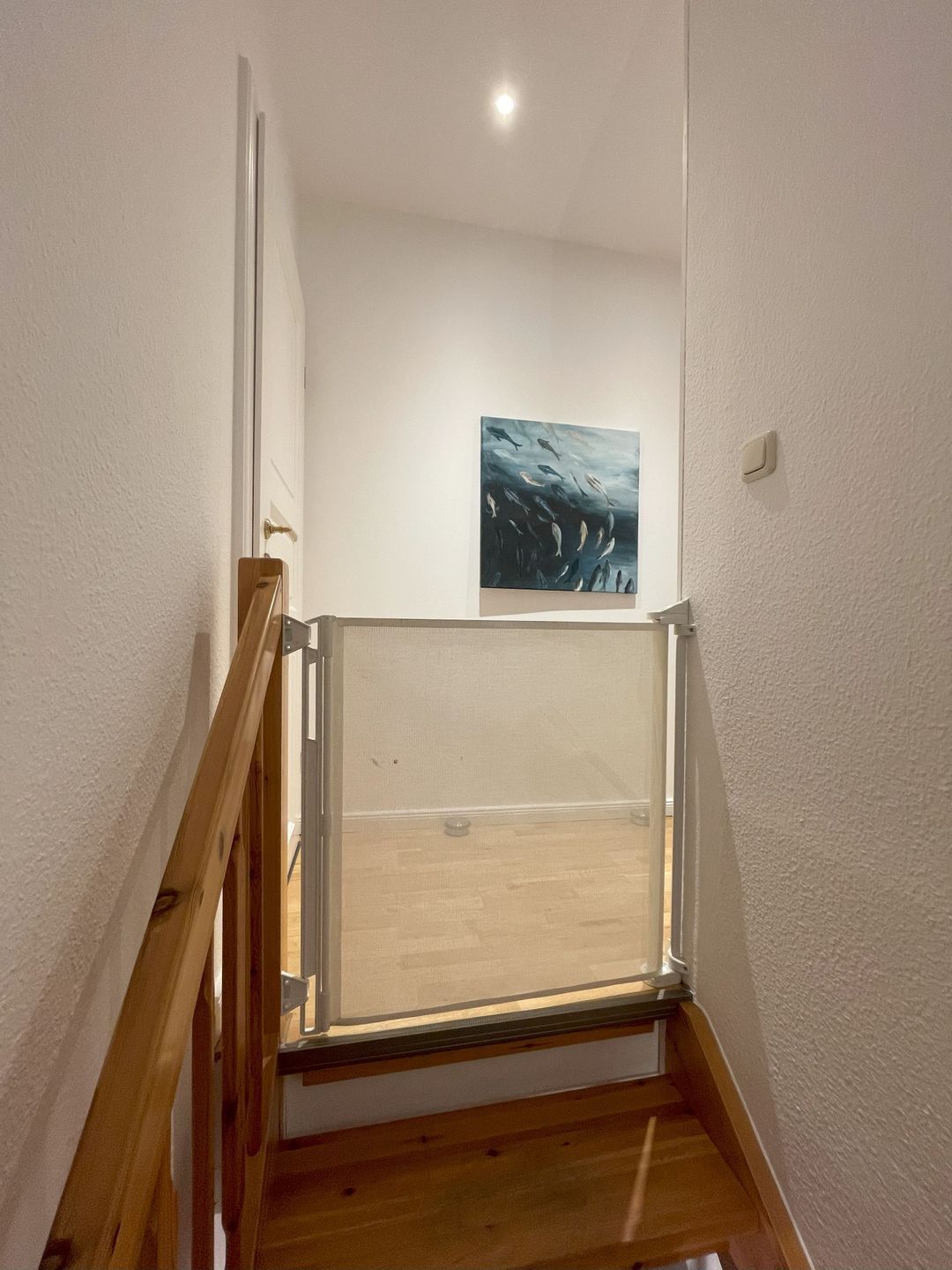 A staircase with a wooden handrail, a glass balustrade, and a painting on the wall.