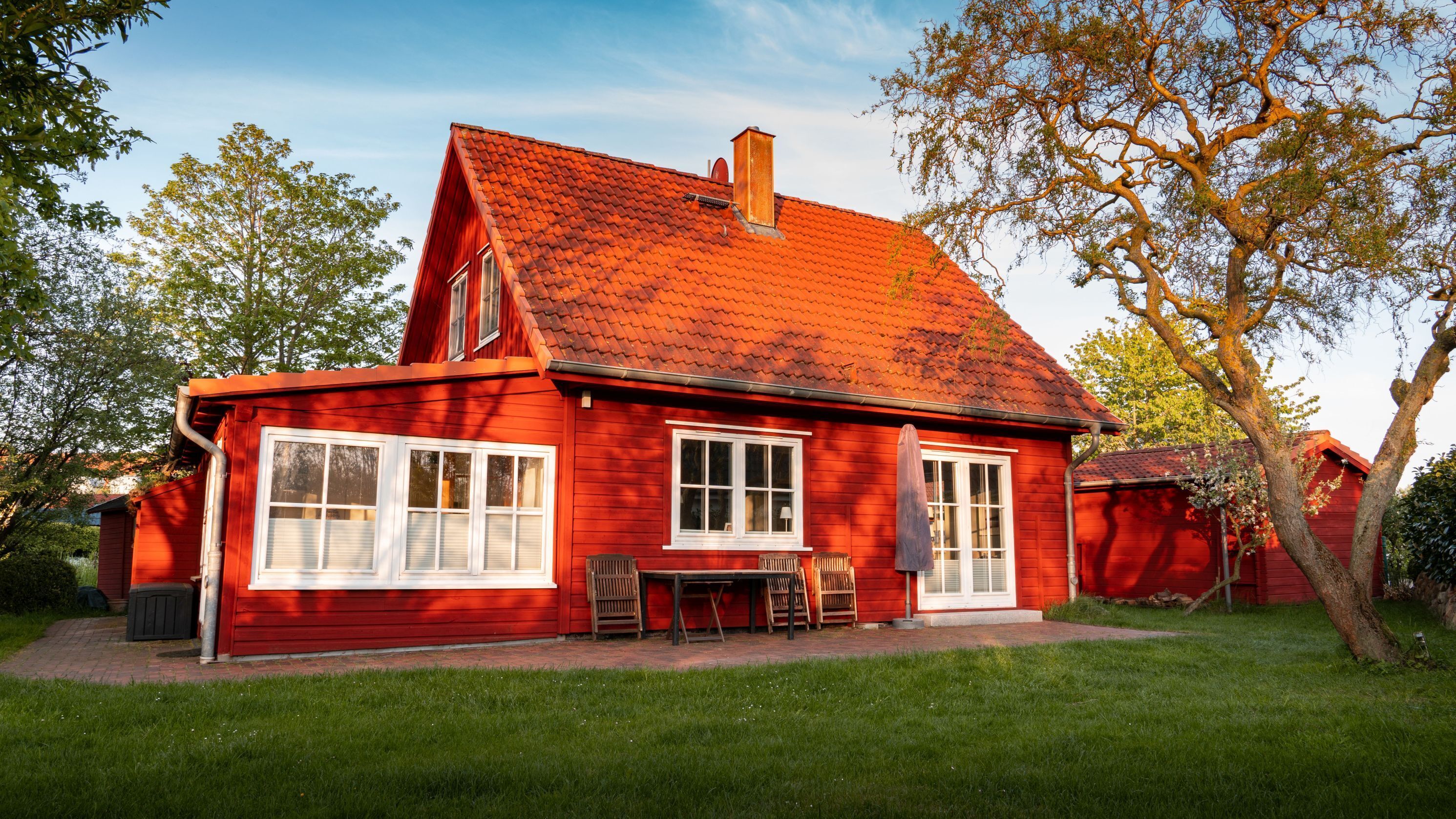 Ein rotes Haus mit geneigtem Dach, großen Fenstern und einer Terrasse.