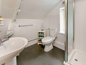 Ein Badezimmer mit weißem Waschbecken, Toilette und Dusche. Handtuchhalter, Heizkörper und ein Regal mit Handtüchern sind ebenfalls vorhanden.