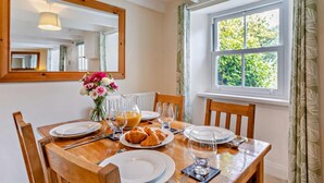 Uma mesa de jantar posta com pratos, copos e croissants, com uma janela e cortinas ao fundo.