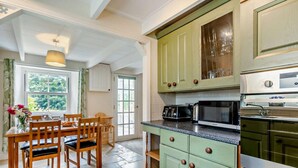 Uma cozinha com armários verdes, uma mesa de jantar com cadeiras, micro-ondas e máquina de lavar louça.