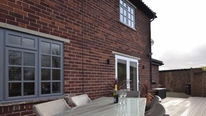 A patio with a glass-top table and chairs, a bottle of champagne, and a door to a brick building. - 3 Bed in York (oc-hh015) (Tockwith)