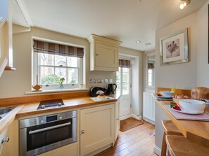 A kitchen with a built-in oven, a window with blinds, a radiator, and a dining table with breakfast items. - 1 Bed in Bedale (oc-g0044) (Patrick Brompton)
