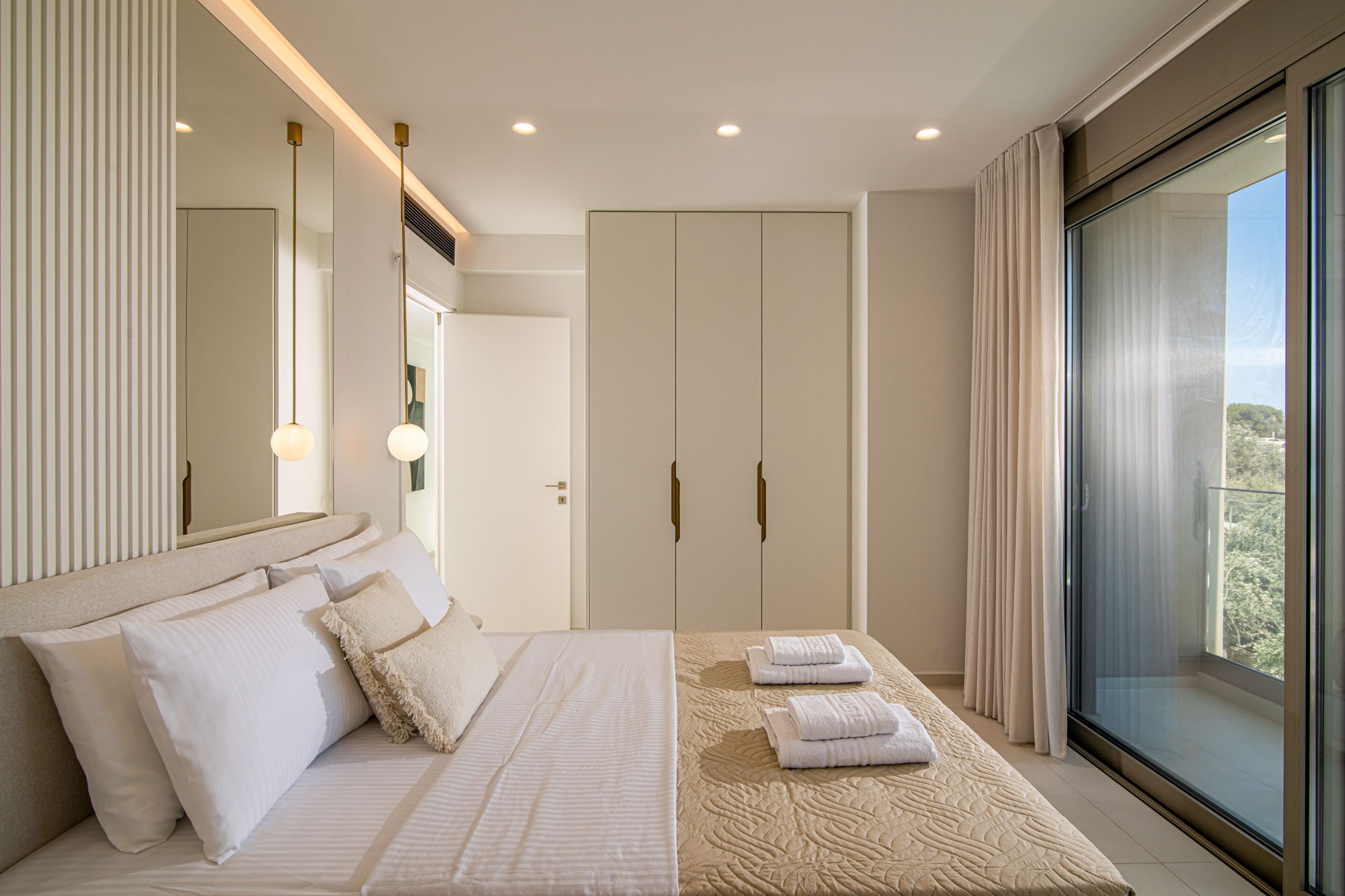 Una habitación de hotel moderna con una cama grande, un armario, un baño y un balcón con vistas.