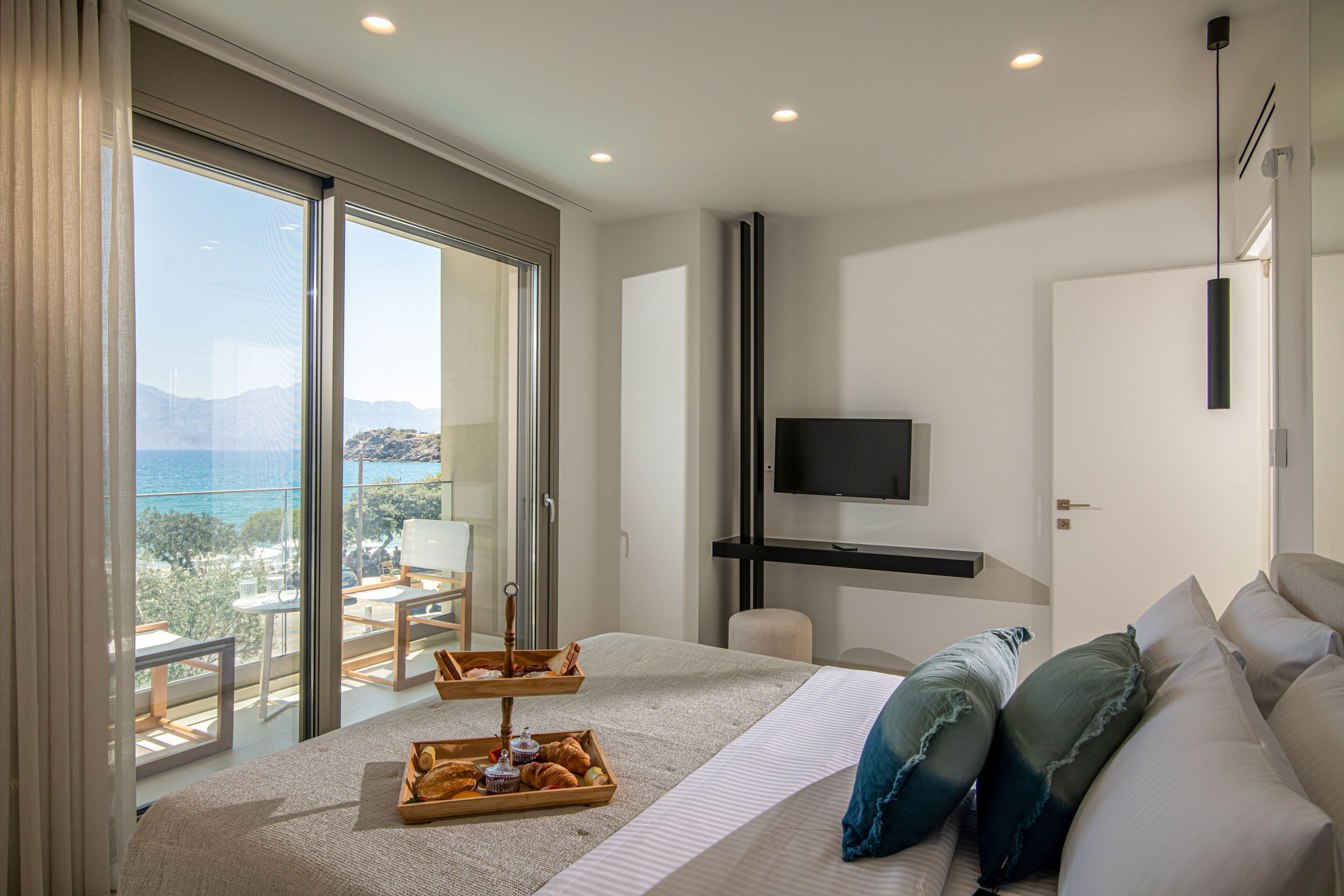 Une chambre d’hôtel avec un grand lit, une télévision, un balcon avec vue et un plateau de petit-déjeuner posé sur le lit.