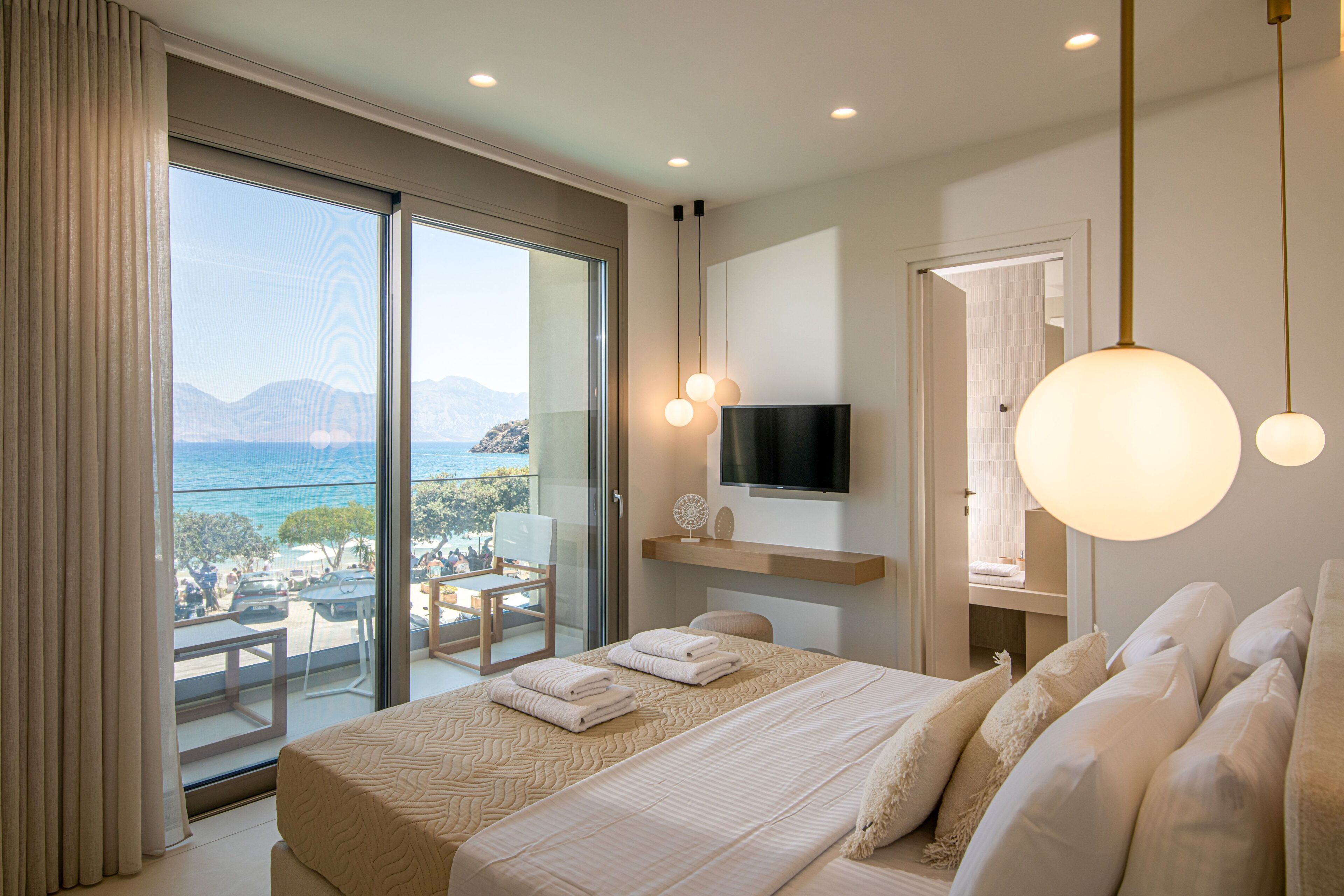 A hotel room with a large bed, a TV, a balcony with a view of the sea, and a dining area.