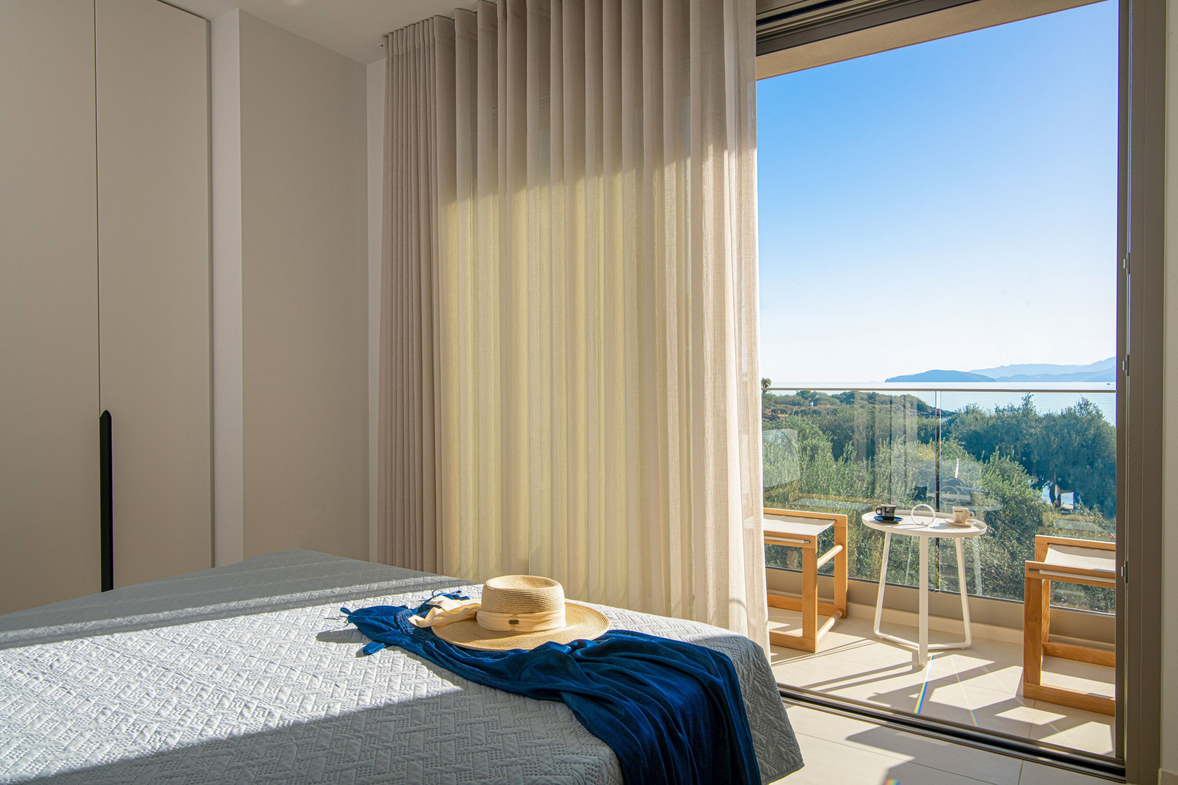 Une chambre d’hôtel avec un lit, un balcon offrant une vue et une table sur laquelle se trouvent un chapeau et une tasse.