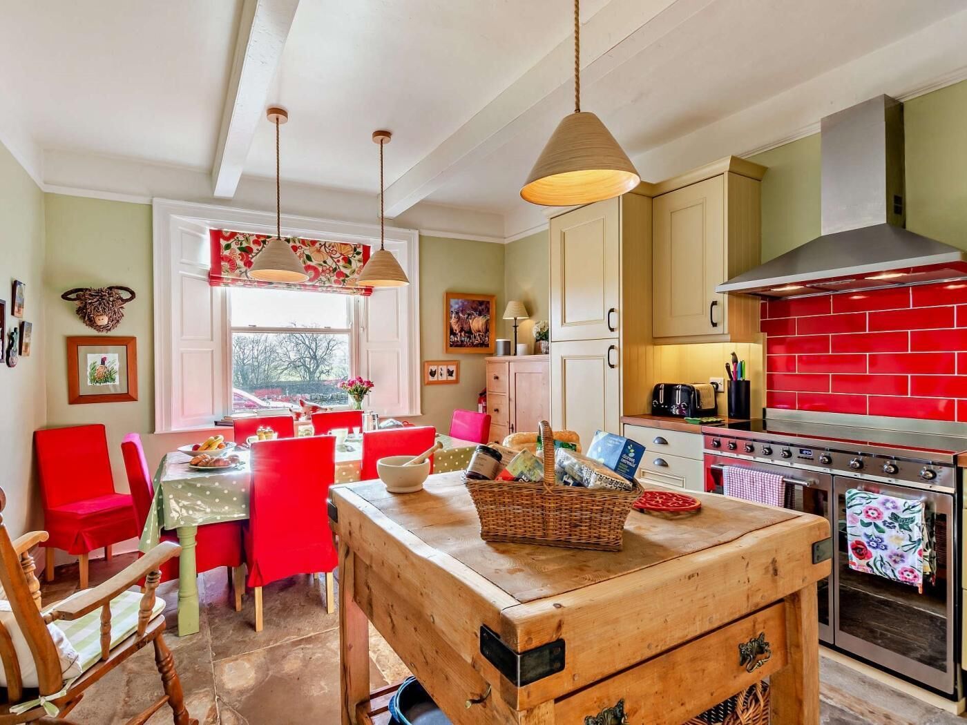 A kitchen with a red tiled backsplash, wooden cabinets, a stove, and a dining area with red chairs and a table.