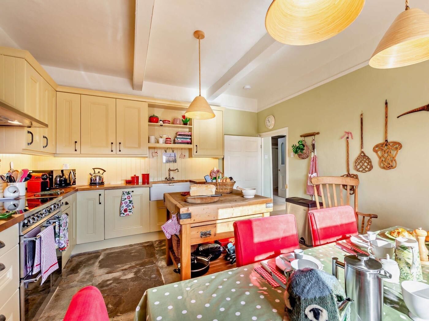 A cozy kitchen with wooden cabinets, a dining table with chairs, a hanging light fixture, and a wall-mounted clock.