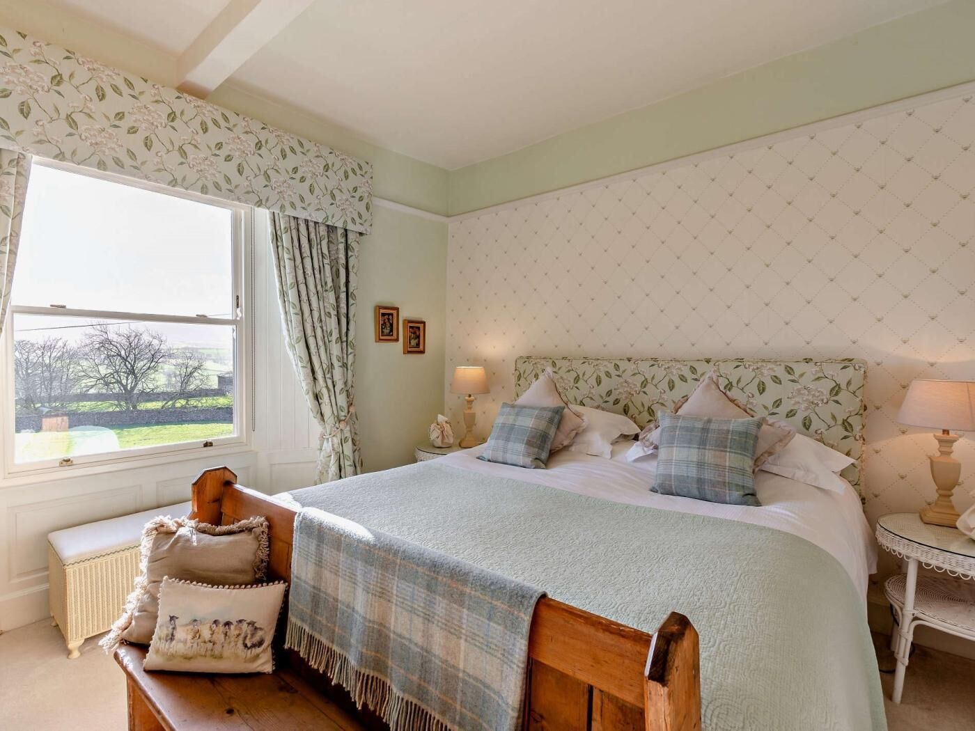 A bedroom with a large bed, a window with curtains, a bedside table, and a bench.