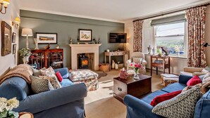 Una sala de estar acogedora con chimenea, sofás azules, televisor y vistas al campo.