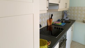 Cuina amb armaris blancs, taule negra, fogó, rentavaixelles i microones.