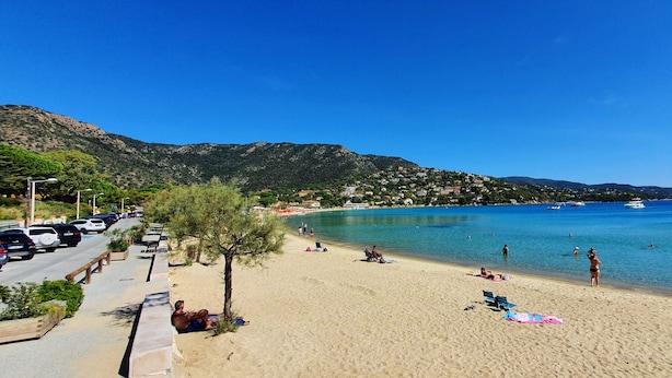 Una platja amb cel blau clar, sorra i poques persones relaxant-se.