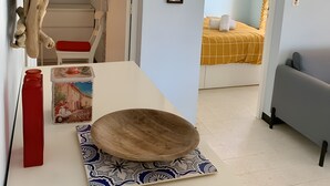 Habitació amb taula blanca, ampolla vermella, bol decoratiu, mirall i llit amb llençol groc.