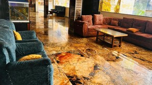 A lobby with a marble floor, blue and brown sofas, a coffee table, and a large window with a view of a temple. - Hotel Nageshwar Palace Rajgir (Rajgir)