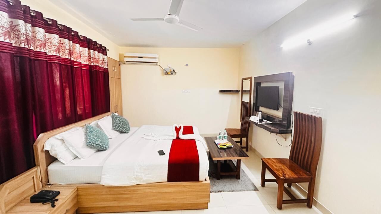 A hotel room with a bed, a desk, a chair, a television, and an air conditioning unit.