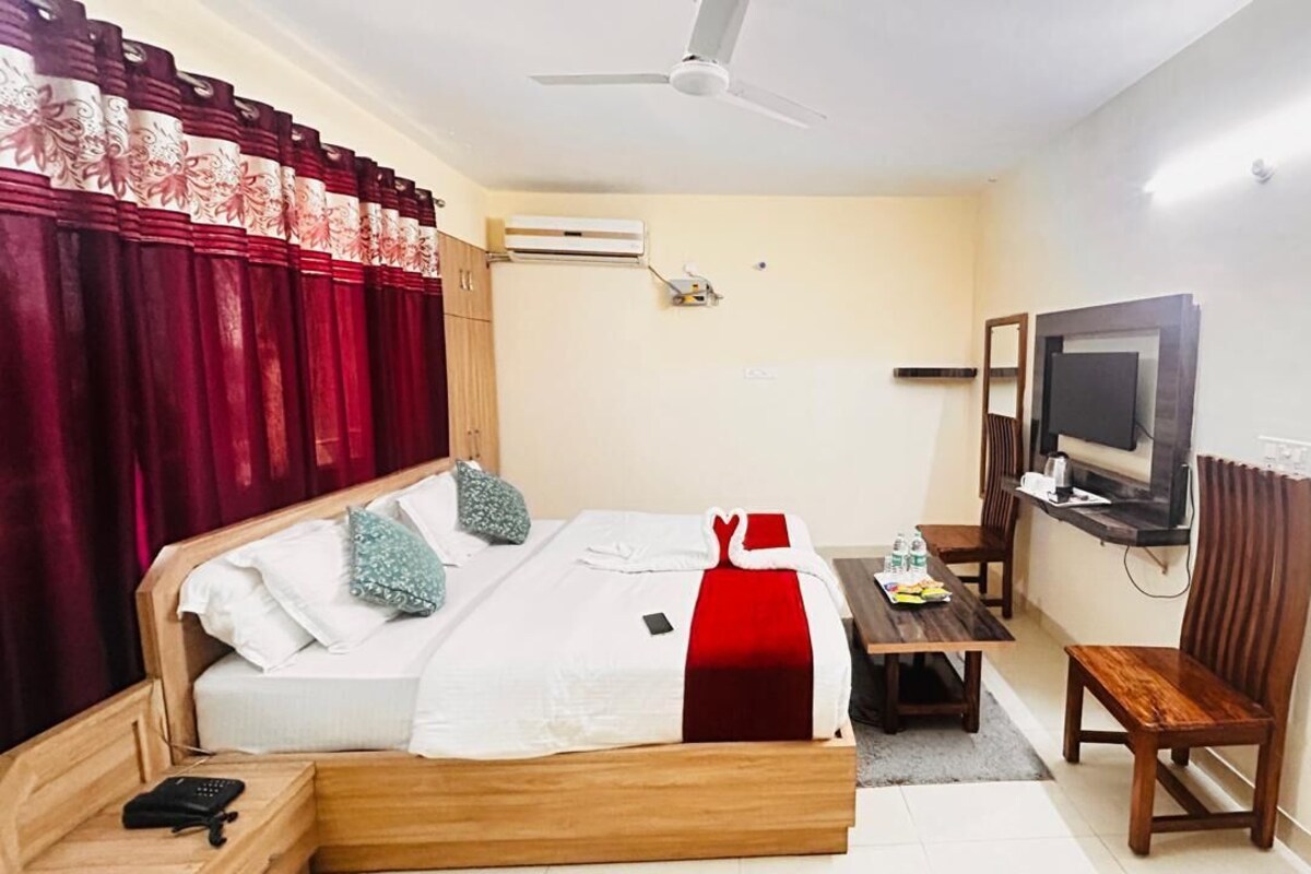 A hotel room with a bed, a desk, a chair, a television, and an air conditioning unit.