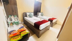 A hotel room with two beds, a wooden headboard, a small table with snacks, and a water dispenser. - Hotel Nageshwar Palace Rajgir (Rajgir)