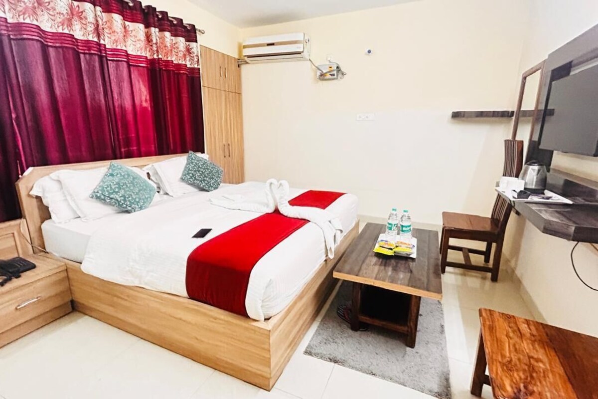 A hotel room with a bed, bedside table, TV, and a desk with a chair.