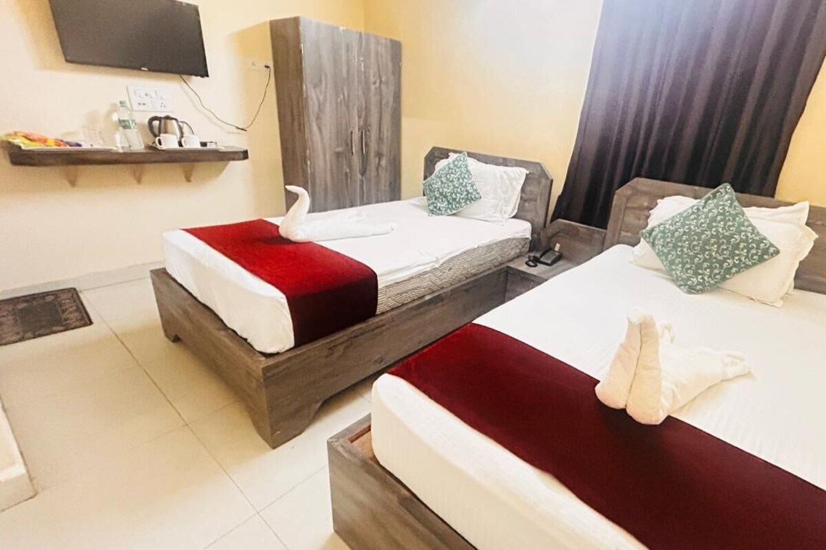 Two beds with red and white bedding, a wooden wardrobe, a television on the wall, and a shelf with toiletries.