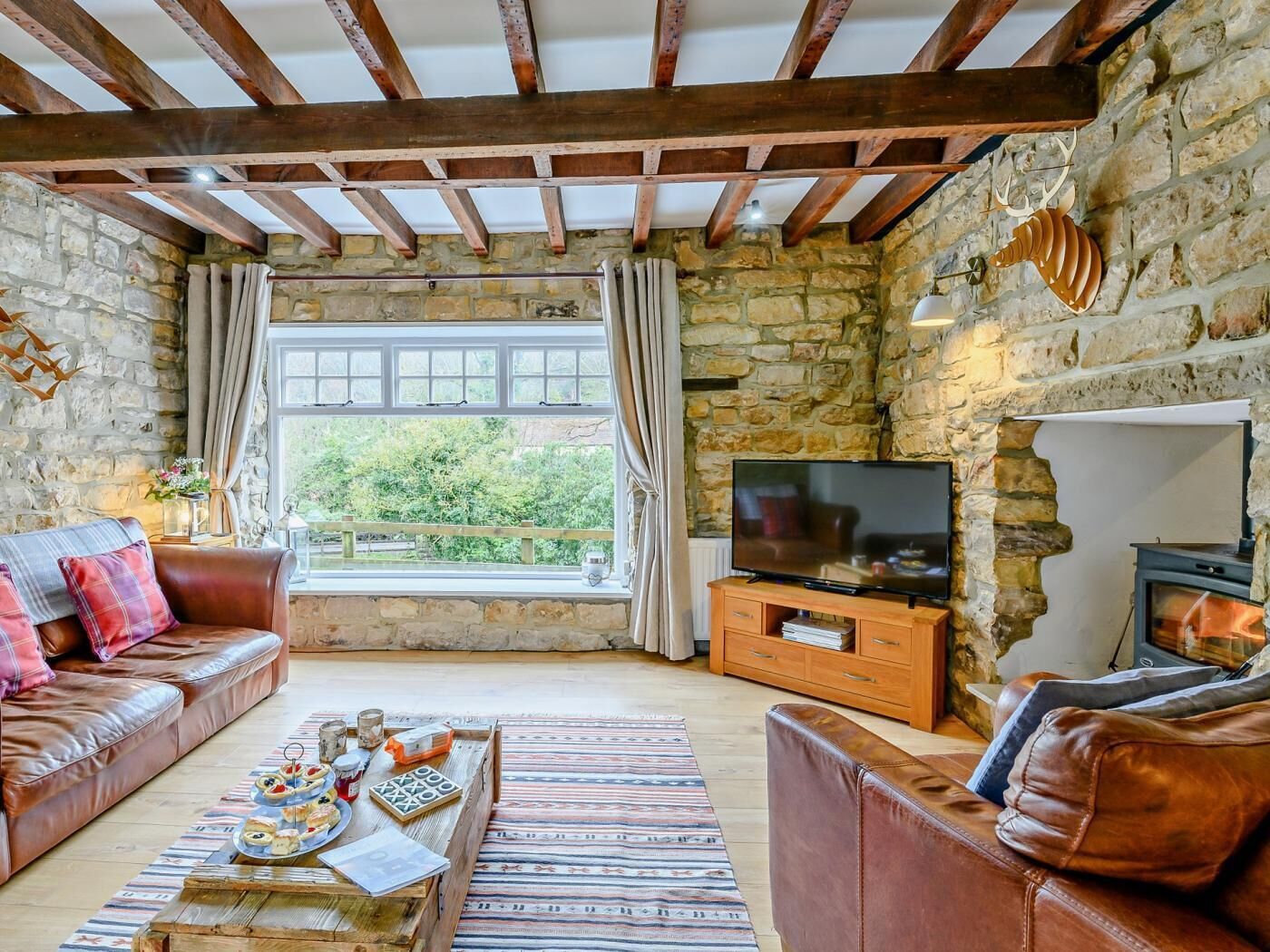 Ein gemütliches Wohnzimmer mit Steinwänden, einer Holzbalkendecke, einem Fernseher und einem Kamin.