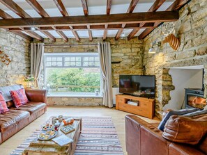 Ein gemütliches Wohnzimmer mit Steinwänden, einer Holzbalkendecke, einem Fernseher und einem Kamin.
