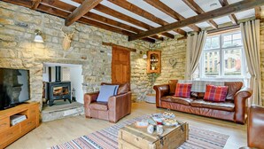 Ein gemütliches Wohnzimmer mit Steinwänden, Holzbalken, einem Kamin, Ledersofas und einem Fernseher.