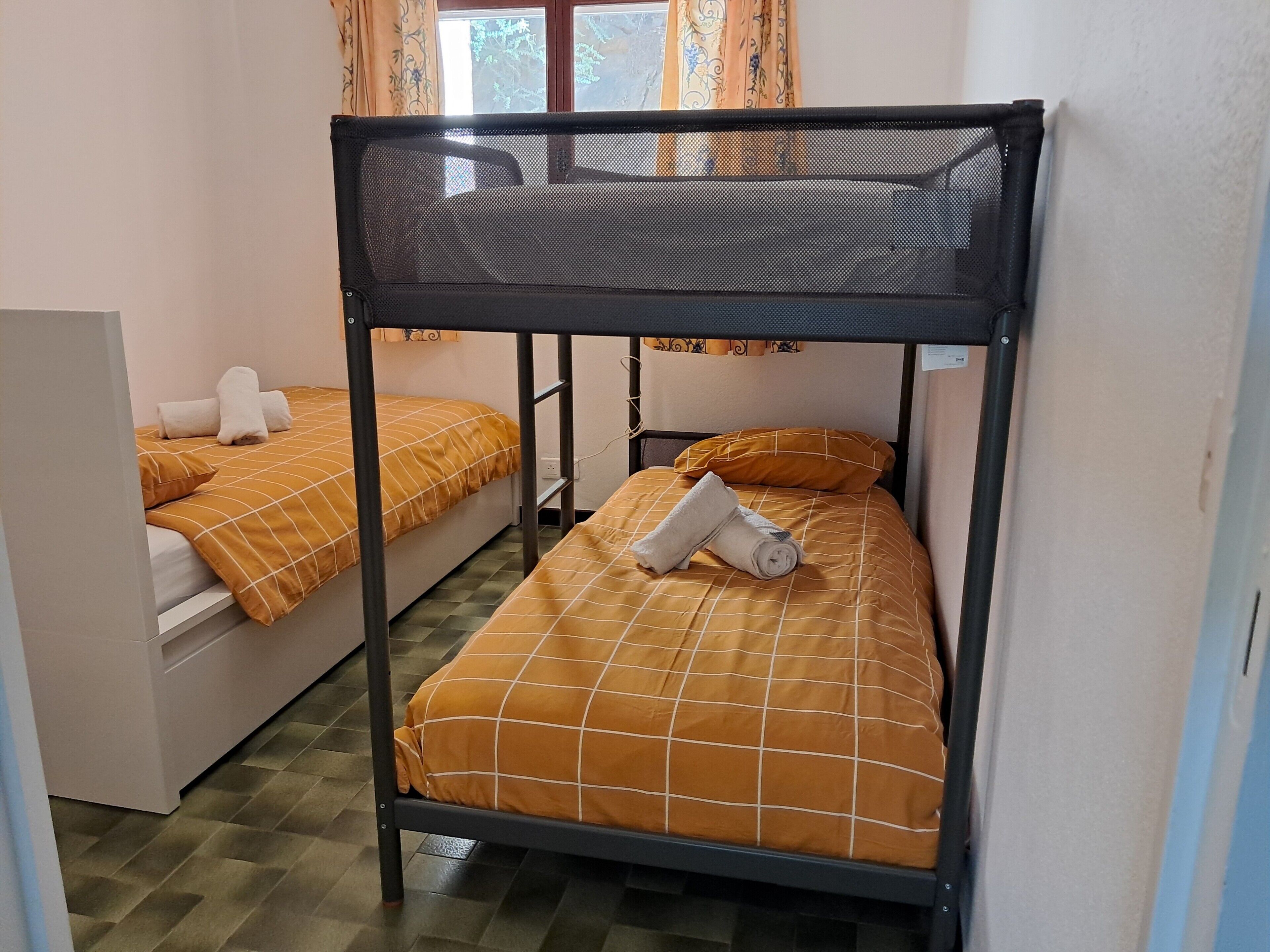 Kerrossängyllä varustettu huone, jossa on kaksi sänkyä. Jokaisessa sängyssä on pääty ja rullalle taitettu pyyhe.