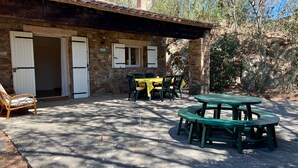 A stone building with a tiled roof, a covered patio with a table and chairs, and a door with shutters. - Domaine Anoutous, Carry – Peaceful Vacation Home Close to the Beach (Le Lavandou)