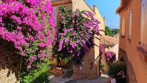 A narrow street with buildings, a stone staircase, and vibrant pink bougainvillea. - Domaine Anoutous, Carry – Peaceful Vacation Home Close to the Beach (Le Lavandou)
