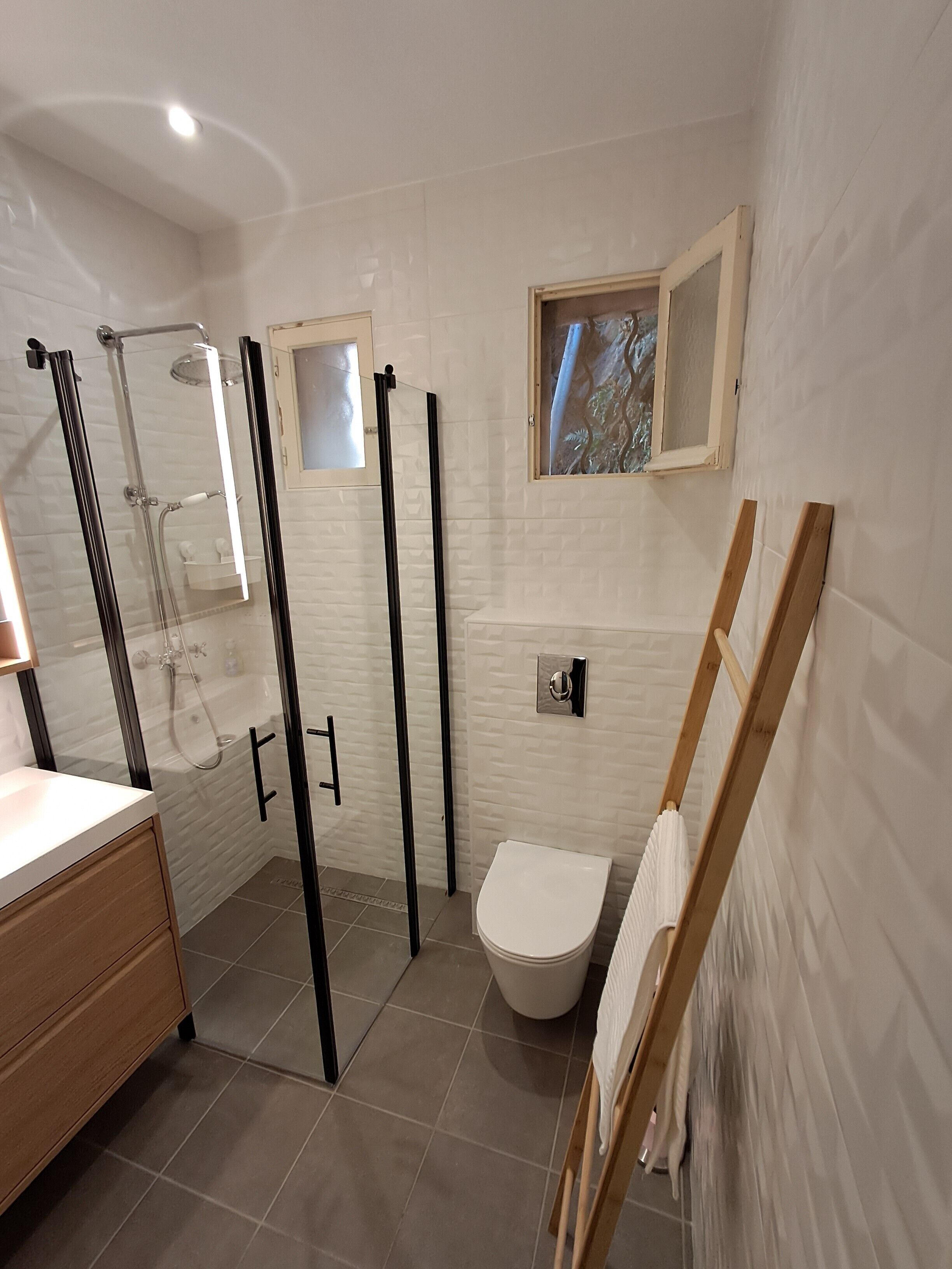 A modern bathroom with a glass-enclosed shower, a white toilet, and a wooden bench.
