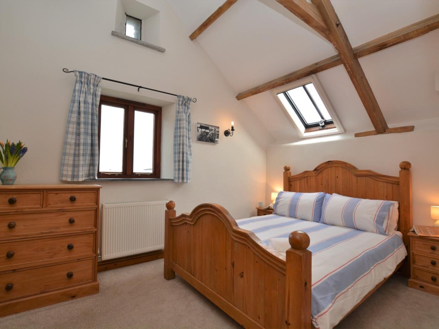 A bedroom with a wooden bed, a dresser, a window with curtains, a skylight, and a radiator.