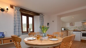 Un coin repas comprenant une table ronde en bois, quatre chaises en bois, un vase avec des fleurs et une fenêtre avec des rideaux.