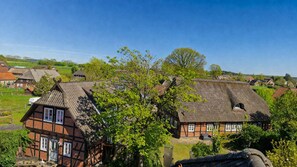 A traditional half-timbered house with a thatched roof, surrounded by lush greenery and other houses. - Charming Vacation Rental in a Half-Timbered House (Egestorf)