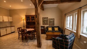 A cozy living room with a plaid sofa, wooden dining table, and chairs. There is a kitchen area with cabinets and a radiator. - Charming Vacation Rental in a Half-Timbered House (Egestorf)