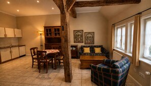A cozy living room with a plaid sofa, wooden dining table, and chairs. There is a kitchen area with cabinets and a radiator. - Charming Vacation Rental in a Half-Timbered House (Egestorf)