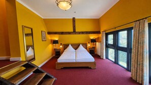 Een kamer met een groot bed, twee nachtkastjes met lampen, een spiegel en een raam met gordijnen.