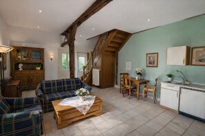 A cozy living room with a sofa, a coffee table, and a staircase leading to a kitchen area. - Charming Vacation Rental in a Half-Timbered House (Egestorf)