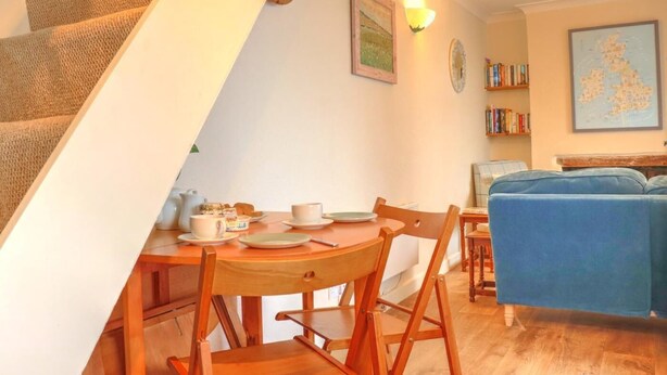 Ein gemütlicher Wohnbereich mit Treppe, einem Esstisch mit Stühlen, einem blauen Sofa, einem Bücherregal und einer Karte an der Wand.
