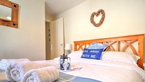 Ein ordentlich bezogenes Bett mit einer blauen und weißen Bettdecke, einer herzförmigen Wanddekoration und einem Kissen mit dem Aufdruck 'Sail Away With Me'.