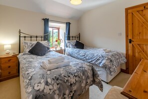 A bedroom with two beds, a wooden door, and a nightstand with a lamp. - 3 Bed in Bodmin (oc-ltbra) (Cardinham)